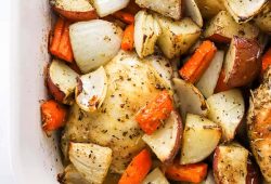 Roasted chicken thighs over potatoes, onion and carrots in a baking dish