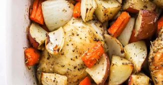 Roasted chicken thighs over potatoes, onion and carrots in a baking dish