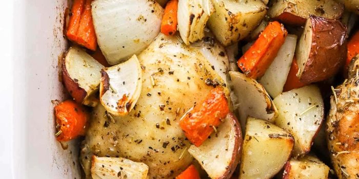 Roasted chicken thighs over potatoes, onion and carrots in a baking dish