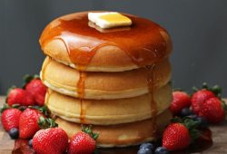 Tall stack of fluffy pancakes with maple syrup, butter and berries