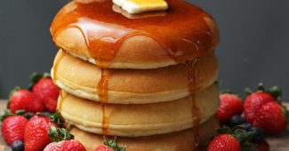 Tall stack of fluffy pancakes with maple syrup, butter and berries