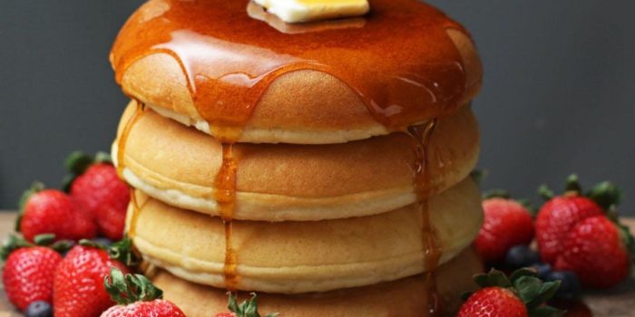 Tall stack of fluffy pancakes with maple syrup, butter and berries