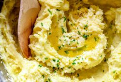 Creamy mashed potatoes in a pot with melted butter and chives