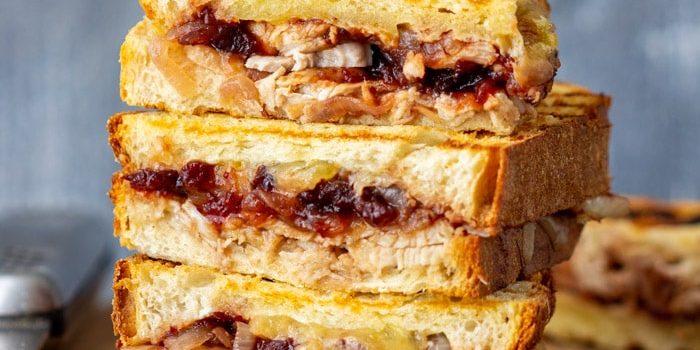 Grilled turkey cranberry panini halves stacked on a wooden board