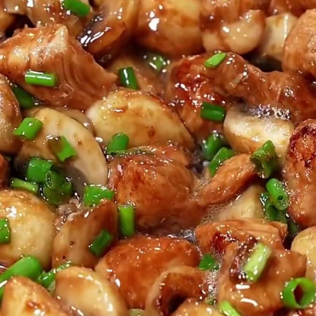 Glossy chicken and mushroom stir fry with whole garlic cloves and chopped green onions in a pan