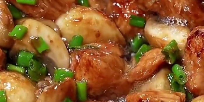Glossy chicken and mushroom stir fry with whole garlic cloves and chopped green onions in a pan
