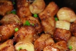 Golden air fryer chicken breast bites with roasted garlic cloves, sesame seeds and green onion in the air fryer basket