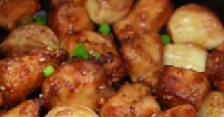 Golden air fryer chicken breast bites with roasted garlic cloves, sesame seeds and green onion in the air fryer basket