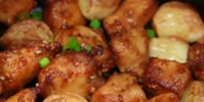 Golden air fryer chicken breast bites with roasted garlic cloves, sesame seeds and green onion in the air fryer basket