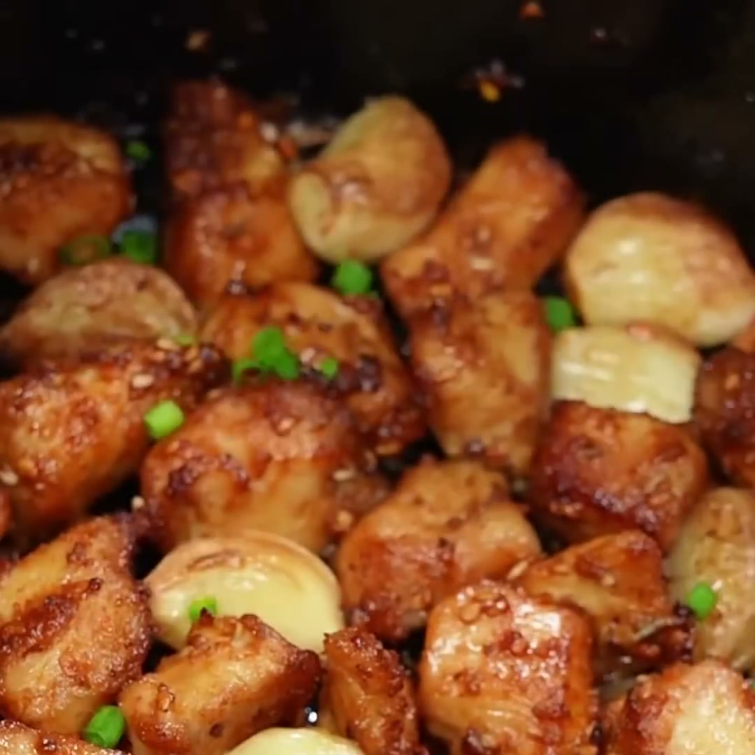 Golden air fryer chicken breast bites with roasted garlic cloves, sesame seeds and green onion in the air fryer basket
