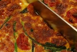Baked eggs with cherry tomatoes, spinach and melted mozzarella being sliced