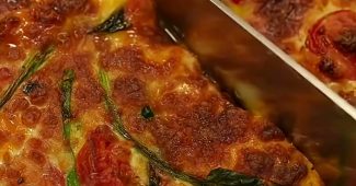 Baked eggs with cherry tomatoes, spinach and melted mozzarella being sliced