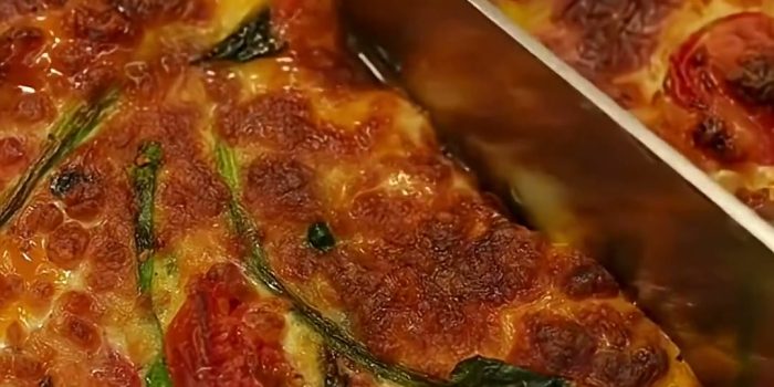 Baked eggs with cherry tomatoes, spinach and melted mozzarella being sliced
