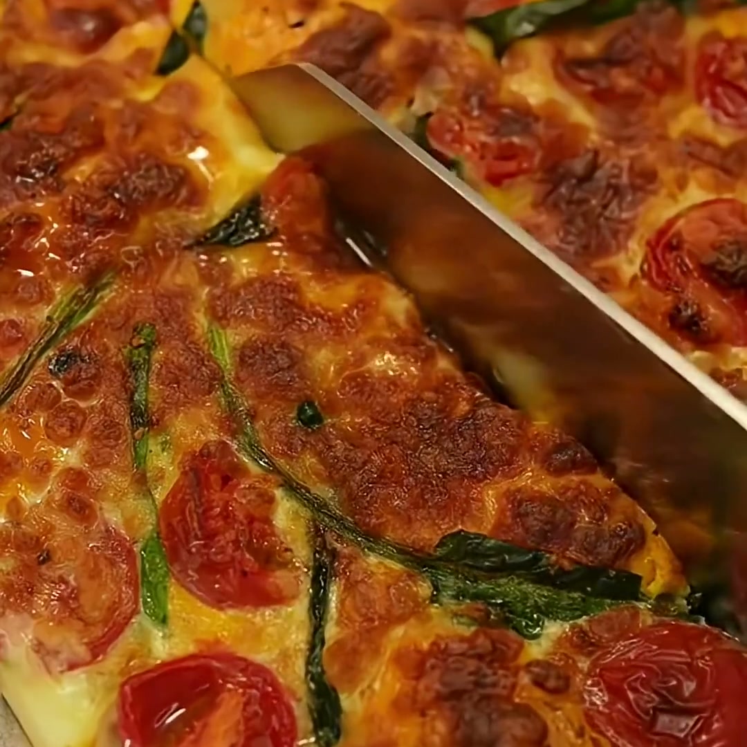 Baked eggs with cherry tomatoes, spinach and melted mozzarella being sliced