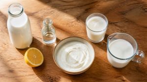 Milk, a halved lemon, white vinegar, plain yogurt, kefir and a measuring cup of milk on a wooden kitchen counter