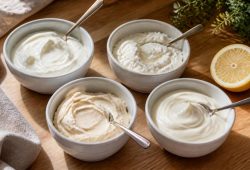 Four small bowls of sour cream substitutes on a wooden counter: Greek yogurt, blended cottage cheese, cashew cream and crème fraîche