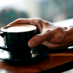 Cup of joe. Hand of a man holding a cup of coffee placed on a table.
