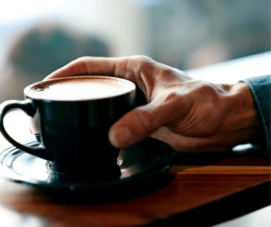 Cup of joe. Hand of a man holding a cup of coffee placed on a table.